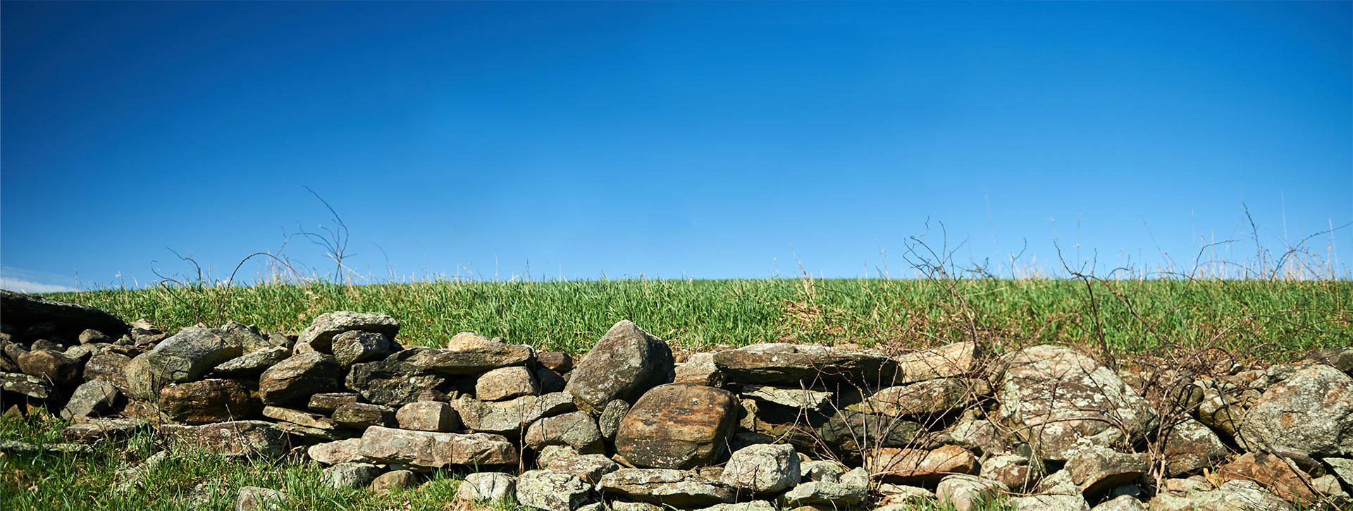 A stone wall in a wide-open field on a sunny day.
